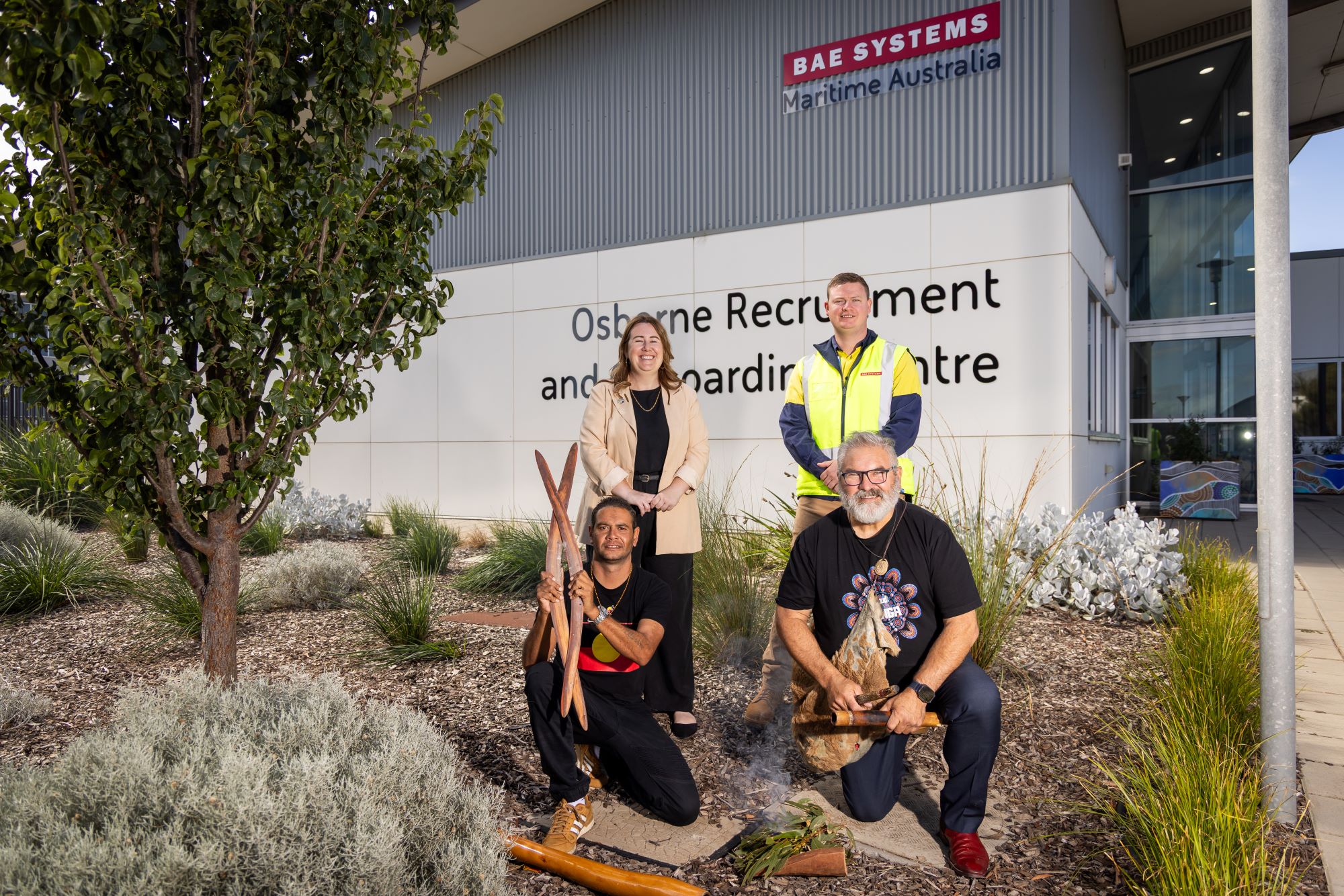 Staff, First Nations partners and colleagues smiling outside of BAE Systems OROC Building at Osborne Naval Shipyard