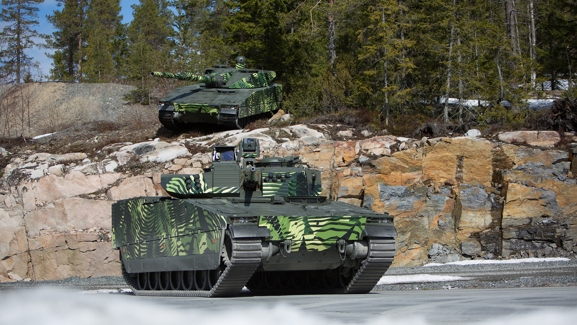 Two green-camouflaged CV90 MkIV combat vehicles. Supreme mobility, exceptional protection, and outstanding lethality.