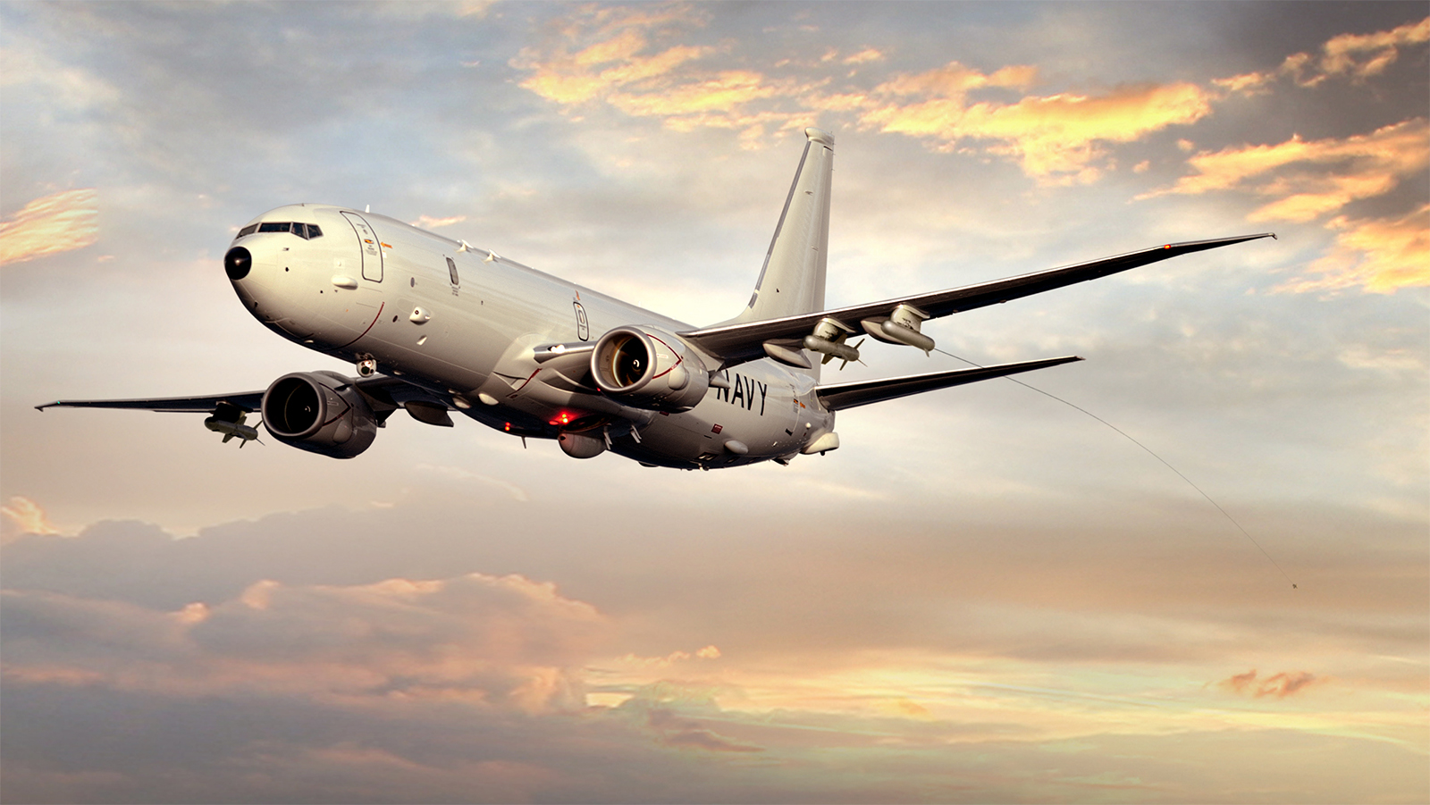 Image shows large P8-A Poseidon Navy aircraft in flight against a dusk sky with thin cloud coverage with attached AN/ALE-55 Fiber-Optic Towed Decoy