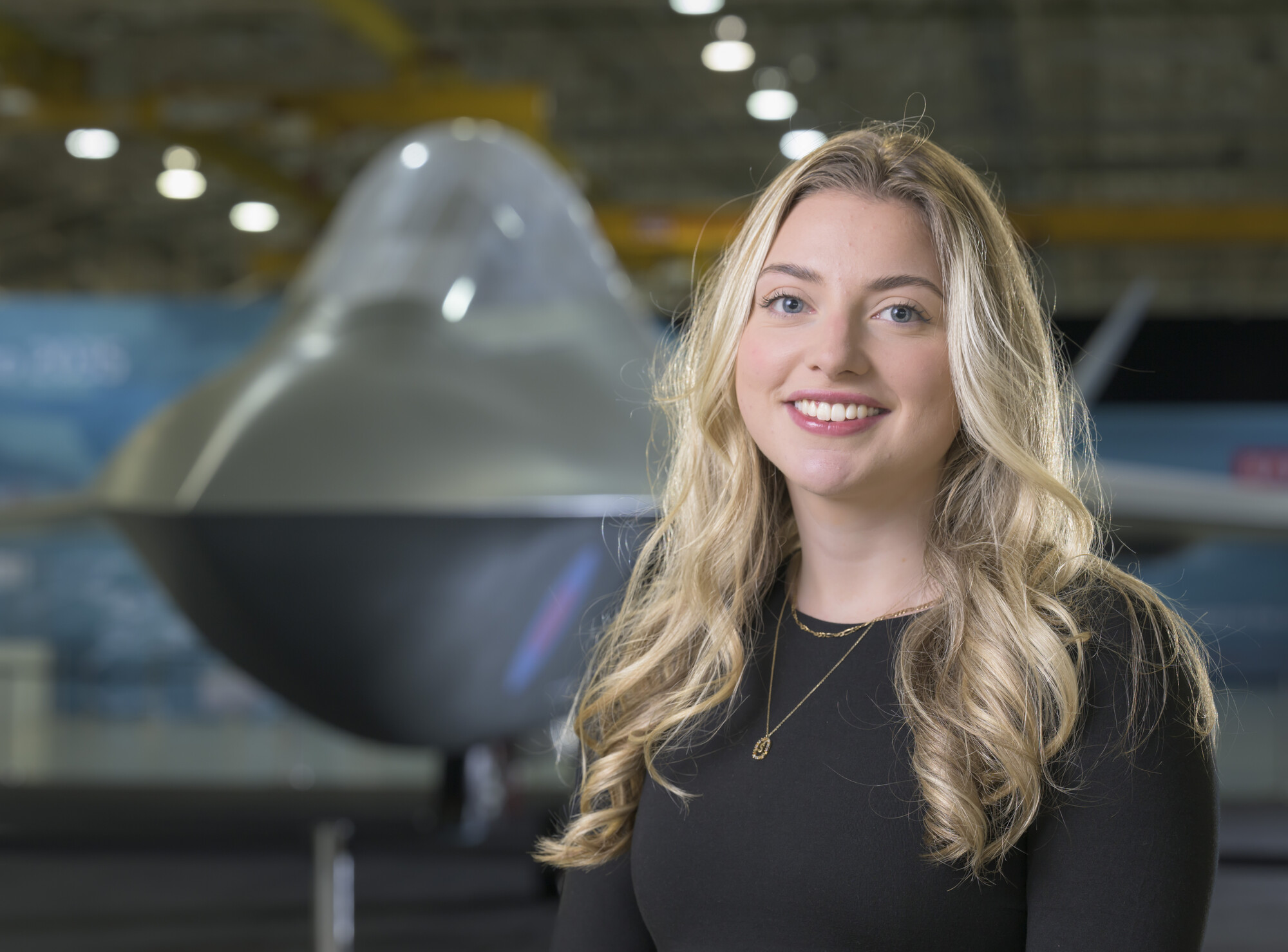 Sarah looking at the camera smiling with the Tempest concept model in the background