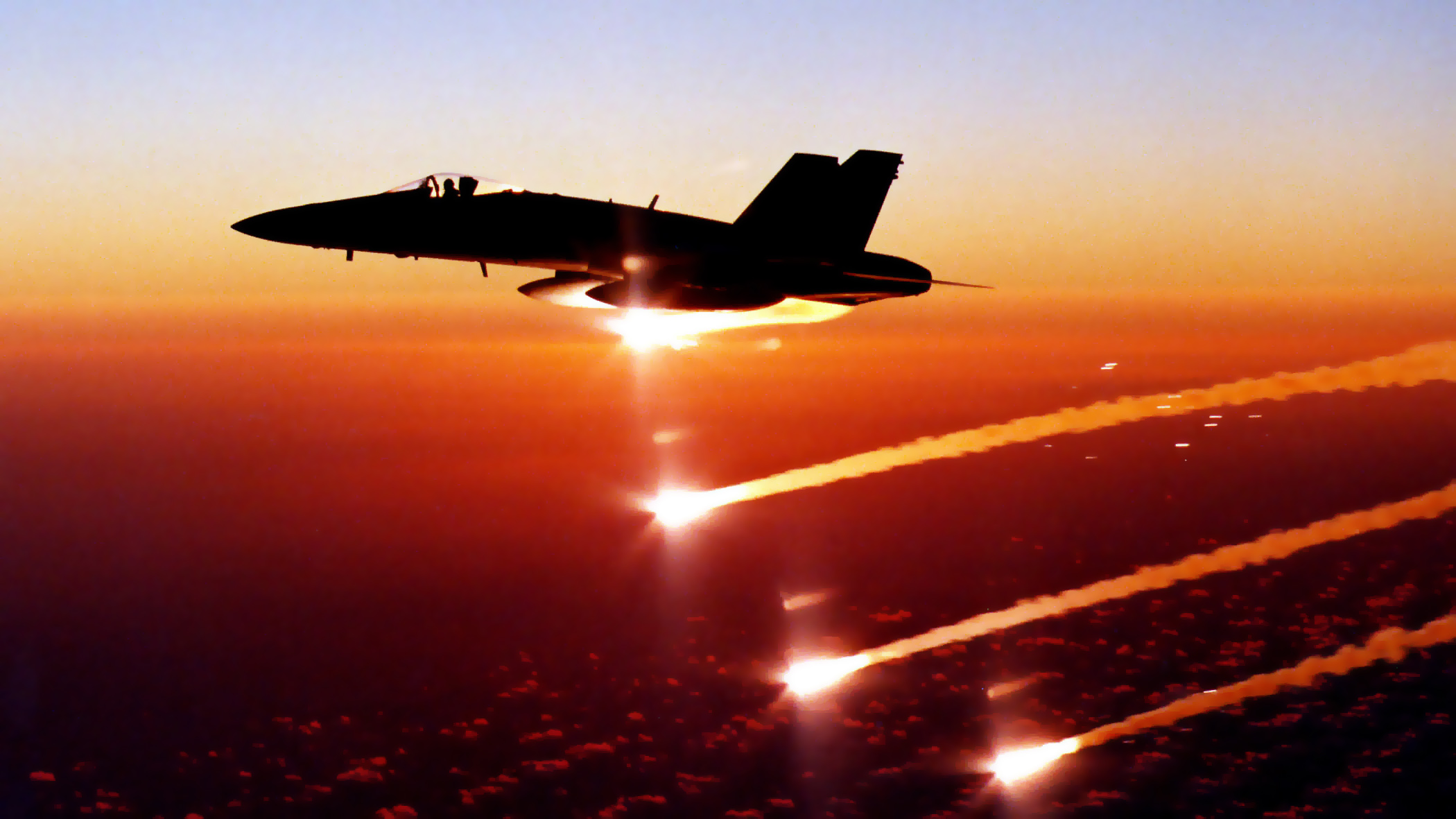 A U.S. Navy F/A-18 Hornet flying at sunset deploys flare countermeasures via the ALE-47 Airborne Countermeasures Dispenser System. 