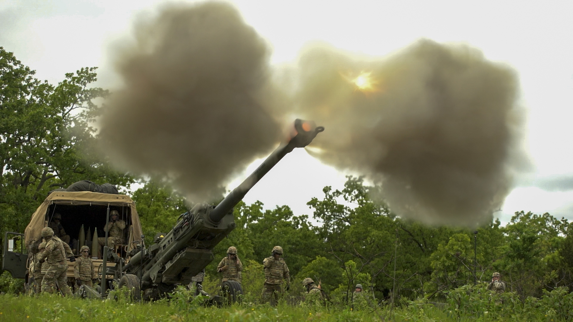 Soldier firing the M777 in a green field on a cloudy day