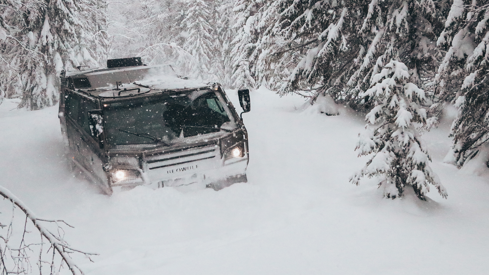 A Beowulf vehicle viewed from the front as it drives through snow-covered woods