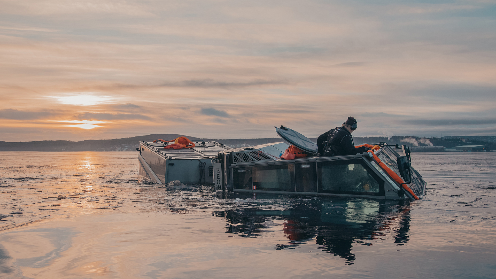 A man climbing out of a Beowulf vehicle in the water at sunrise