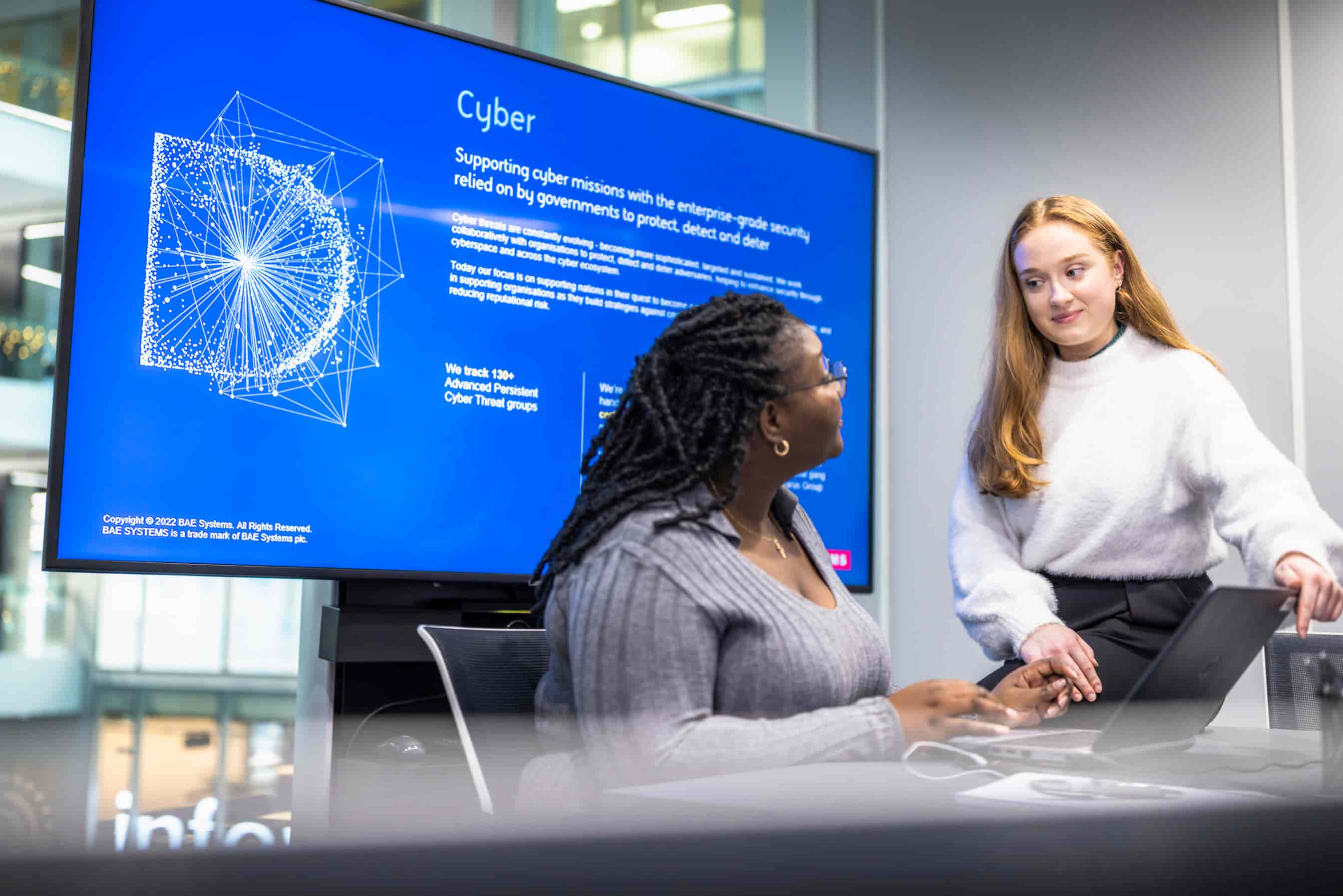 Young women talking in front of huge monitor